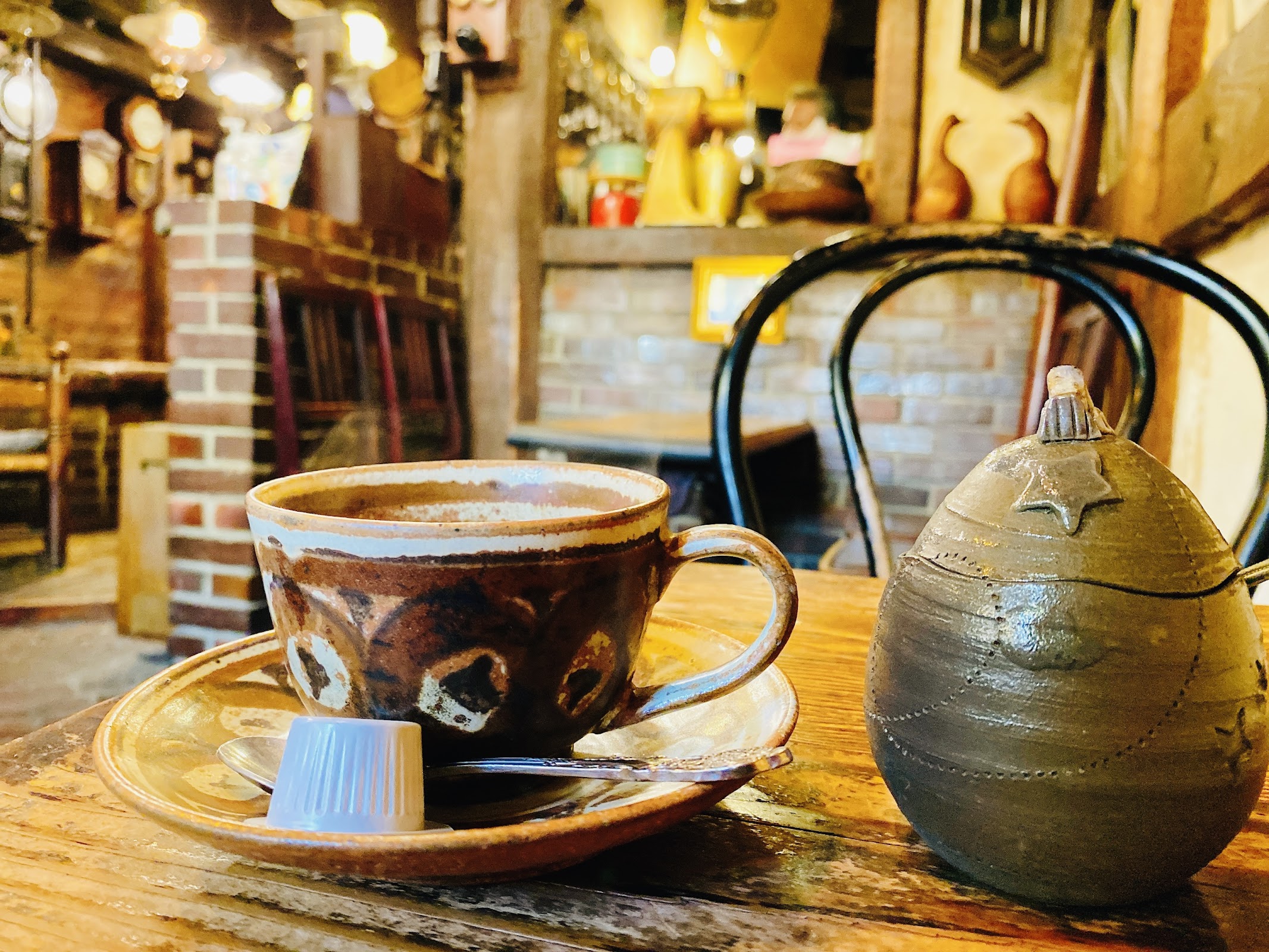 焦げ茶色の釉薬がかかった陶器カップにコーヒーが注がれ、星形模様の陶製シュガーポットが隣に置かれた木製テーブル